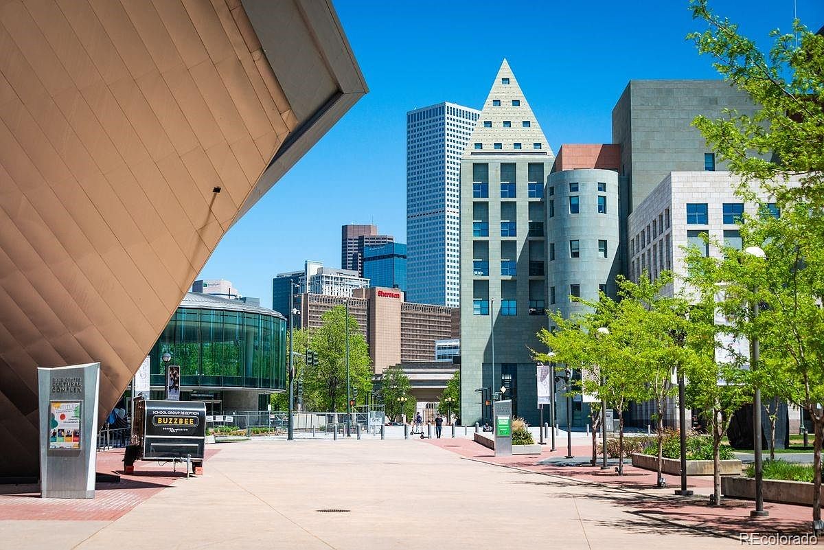 This image showcases a vibrant cityscape with modern architectural designs. The foreground features a pedestrian plaza with well-maintained landscaping and public art installations. The backdrop reveals a mix of high-rise buildings, including the Denver Public Library, creating an impressive urban vista that highlights the city's cultural and commercial appeal.