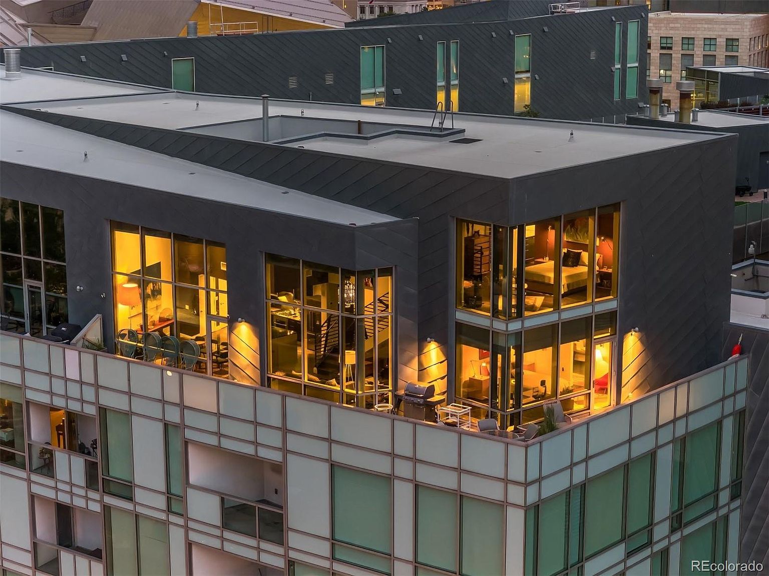 This aerial view showcases a modern residential building with a striking architectural design. The building features a combination of dark gray cladding and large windows, offering ample natural light to the interior spaces. Balconies provide outdoor living areas, and the overall impression is one of contemporary luxury and urban sophistication.