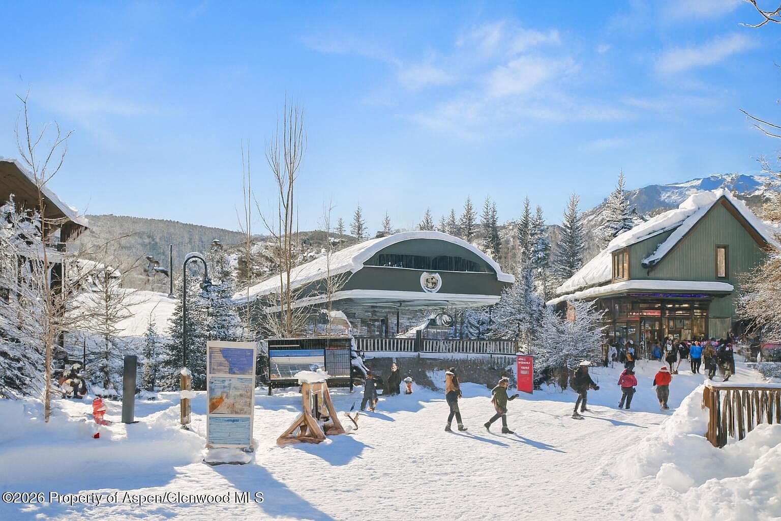 This exterior shot showcases a charming ski resort area covered in snow, featuring a ski lift station and a building with a rustic design. People are seen walking through the snowy landscape, adding a sense of activity and life to the scene. The clear blue sky and snow-covered trees create a picturesque winter setting, perfect for attracting potential buyers interested in a ski resort property.