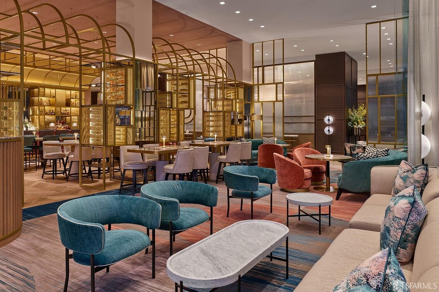 This sophisticated lounge area features a contemporary design with a mix of teal and rust-colored velvet armchairs arranged around stone-topped coffee tables. The space is defined by elegant gold-toned metal arched partitions that create semi-private seating zones and a bar area in the background. The overall aesthetic is upscale and modern, characterized by rich textures, patterned carpeting, and warm, ambient lighting.