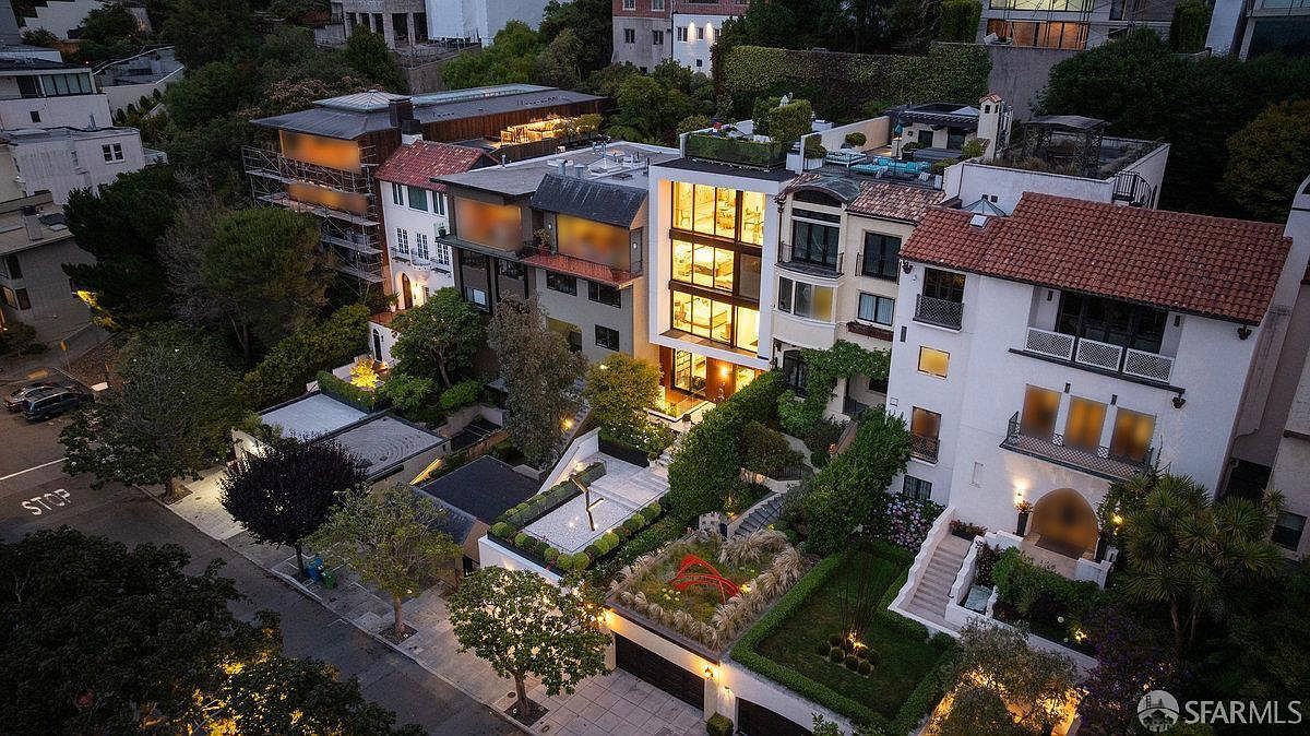 This high-angle aerial perspective captures a sophisticated multi-level residential property nestled within a lush, hilly neighborhood. The architecture features a striking contrast between a modern, glass-fronted central structure with illuminated levels and a more traditional, white-stucco home with a red-tiled roof. Manicured terraced gardens, stone pathways, and vibrant landscaping integrate the buildings into the sloped terrain, creating a luxurious and private urban oasis.