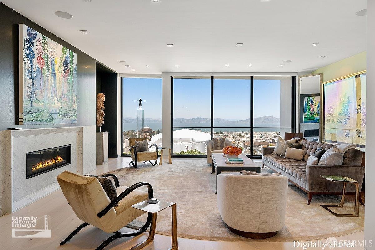 This sophisticated living room features a neutral color palette, a large circular area rug, and a mix of contemporary seating including a tufted sofa and sculptural armchairs. A sleek, linear fireplace is set into a light-toned stone surround, while expansive floor-to-ceiling windows frame a panoramic view of the bay and city skyline. The space is accented by vibrant, large-scale abstract artwork on the walls, creating a refined and artistic atmosphere.