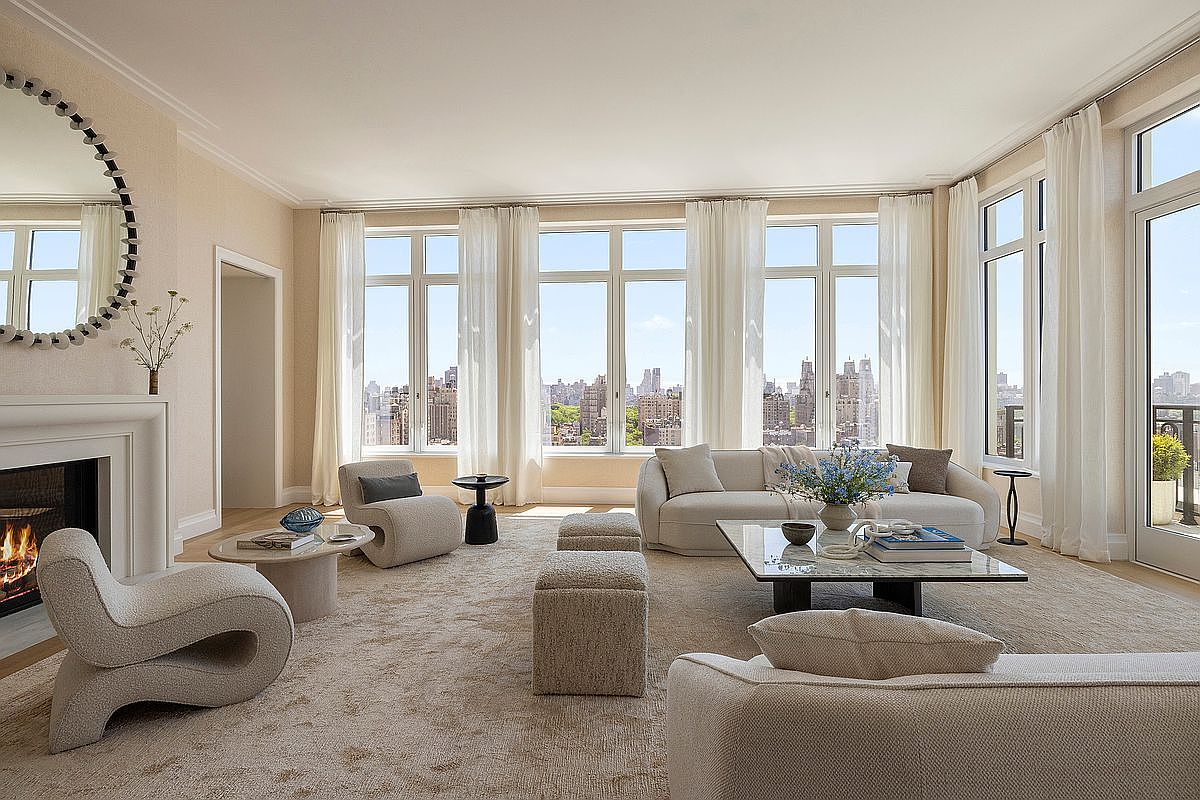 This sophisticated living room features a neutral, monochromatic palette with plush, curved furniture and a textured area rug. A prominent fireplace with a clean-lined surround serves as a focal point, while a wall of large windows provides expansive views of the city skyline and greenery. The space is bathed in natural light, creating an airy and elegant atmosphere suitable for high-end urban living.