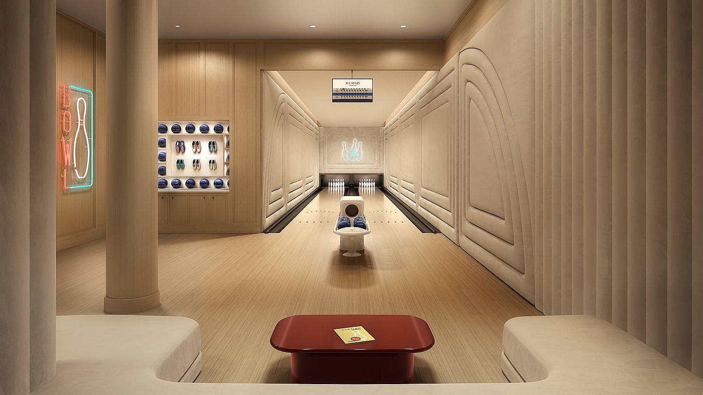 This sophisticated private bowling alley features a sleek, minimalist design with light wood paneling and soft, neutral-toned padded wall accents. The space includes a central bowling lane, a dedicated ball return console, and a recessed display wall showcasing bowling balls, all viewed from a comfortable lounge area with a low-profile red table. The aesthetic is modern and luxurious, creating an exclusive entertainment environment.