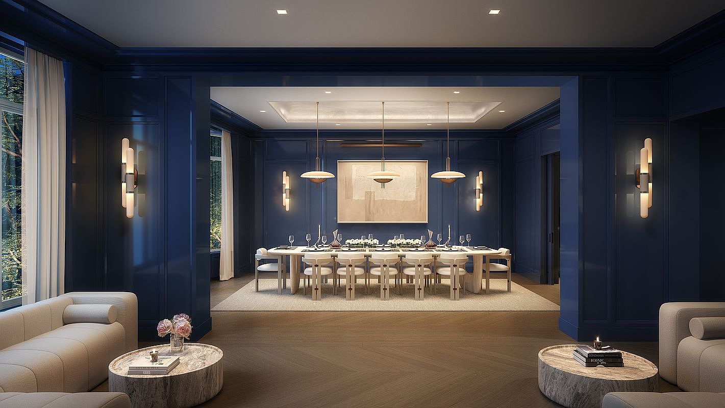 This sophisticated dining room features deep blue paneled walls and a long, central dining table surrounded by light-toned chairs, creating a striking contrast. The space is illuminated by three modern pendant lights hanging above the table, with additional wall sconces providing ambient lighting on either side of a large, framed piece of art. The perspective is centered, looking through a wide opening from a foreground seating area with two round stone-topped tables, emphasizing the open-concept layout and elegant, formal atmosphere.