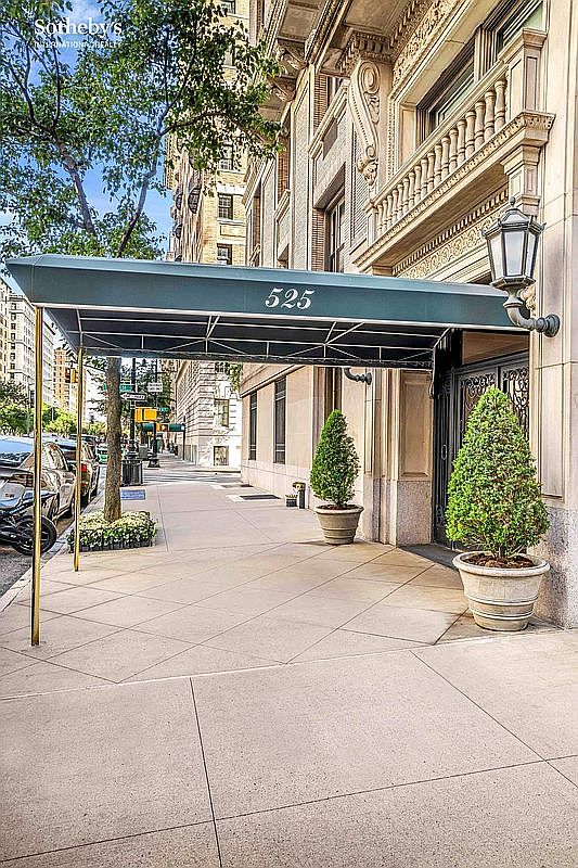 This image showcases the elegant entryway of a building, marked by a dark green awning with the number '525' prominently displayed. Two potted evergreen trees flank the entrance, adding a touch of greenery and sophistication. The building's facade exhibits classic architectural details, suggesting a prestigious and well-maintained property.