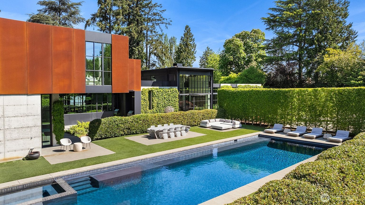 This image showcases a luxurious backyard with a modern architectural home as a backdrop. The focal point is a pristine swimming pool, complemented by lounge chairs and an outdoor dining area. Lush greenery and manicured hedges create a private and serene atmosphere, enhancing the property's appeal.