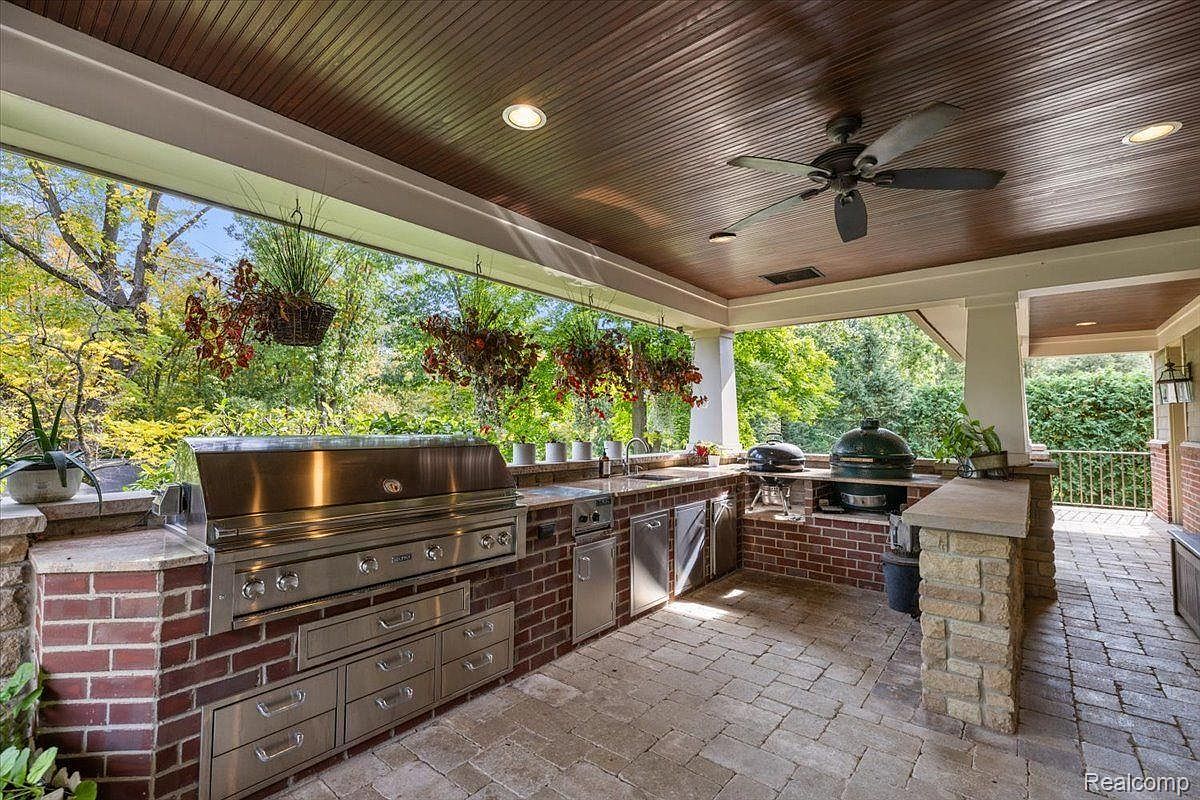 This image showcases a luxurious outdoor kitchen and patio area. The space features a built-in stainless steel grill, brickwork, and ample counter space, perfect for outdoor entertaining. Hanging plants add a touch of nature, while the brick-paved patio provides a classic and elegant feel.