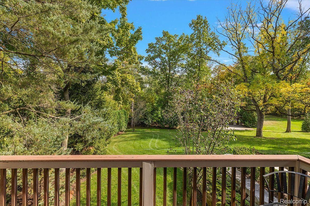 This image showcases a charming outdoor space, specifically a patio or deck, overlooking a lush green yard and garden. The wooden railing of the deck provides a clear view of the well-maintained lawn and mature trees, creating a sense of tranquility and privacy. The scene suggests a perfect spot for relaxation and outdoor entertainment.