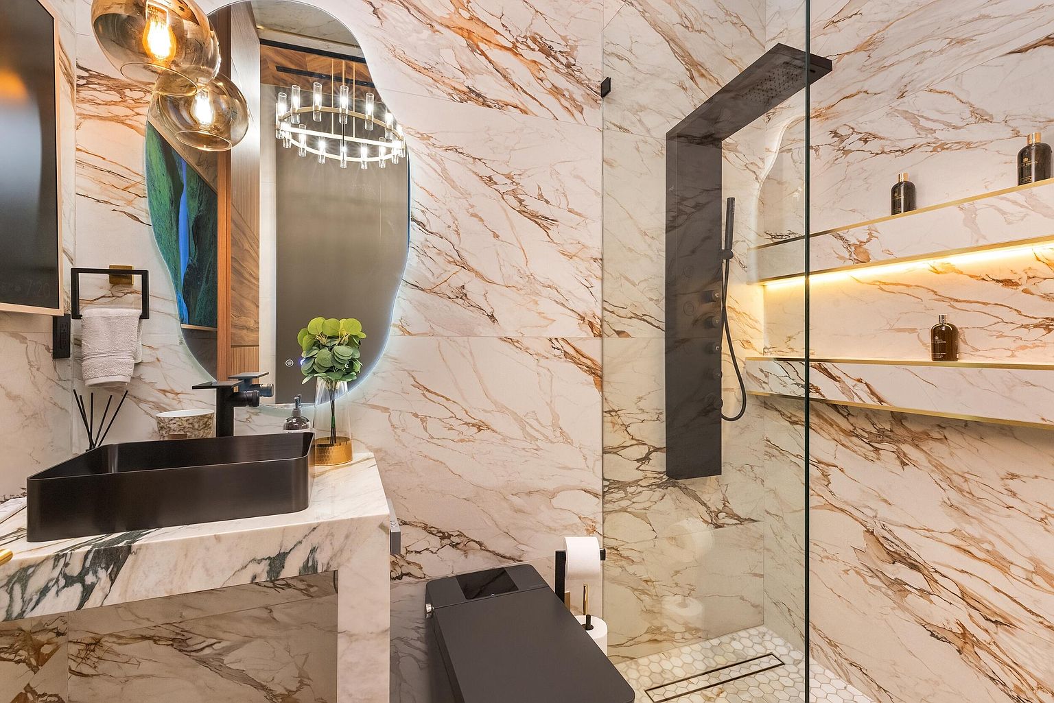 This luxurious bathroom features striking stone walls with bold veining and a sleek, dark-toned vanity with a matching vessel sink. A glass-enclosed shower area includes integrated shelving with warm accent lighting, while a modern, dark-toned toilet sits adjacent to the vanity. The space is accented by a uniquely shaped mirror and contemporary pendant lighting, creating a sophisticated and high-end aesthetic.