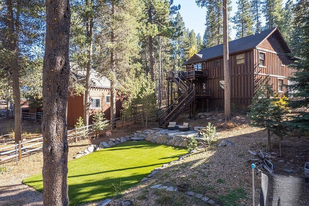 This exterior shot showcases a well-maintained yard with a lush green lawn, complemented by natural landscaping and mature trees. A multi-level wooden house with an elevated deck and staircase is visible in the background, adding architectural interest. The scene evokes a sense of tranquility and privacy, ideal for outdoor living and relaxation.