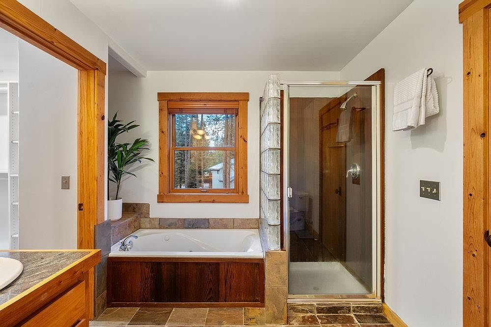 This primary bathroom features a jacuzzi tub with wood paneling, a window with wood trim, and a glass-enclosed shower. The flooring is tiled, and the walls are painted a neutral color. The overall style is rustic and cozy, creating a relaxing atmosphere.
