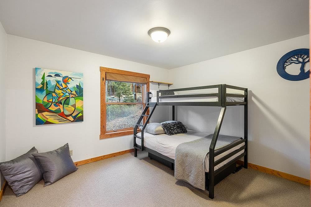 This is a cozy guest bedroom featuring a bunk bed with a dark frame, complemented by neutral-toned bedding and a decorative throw. A colorful abstract painting hangs on the wall, adding a touch of vibrancy to the room. The room is well-lit with natural light from a window, creating a welcoming and comfortable atmosphere.