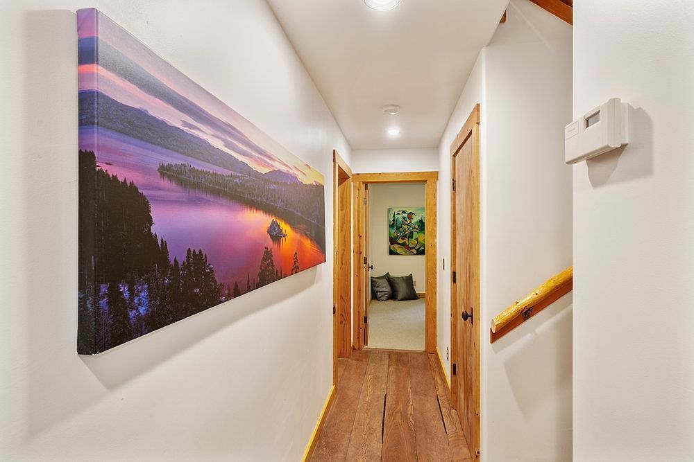 This interior shot showcases a hallway with hardwood flooring and white walls. A large landscape painting adorns the left wall, while wooden doors and trim add warmth to the space. The hallway leads to other rooms, creating a sense of flow and connectivity within the home.