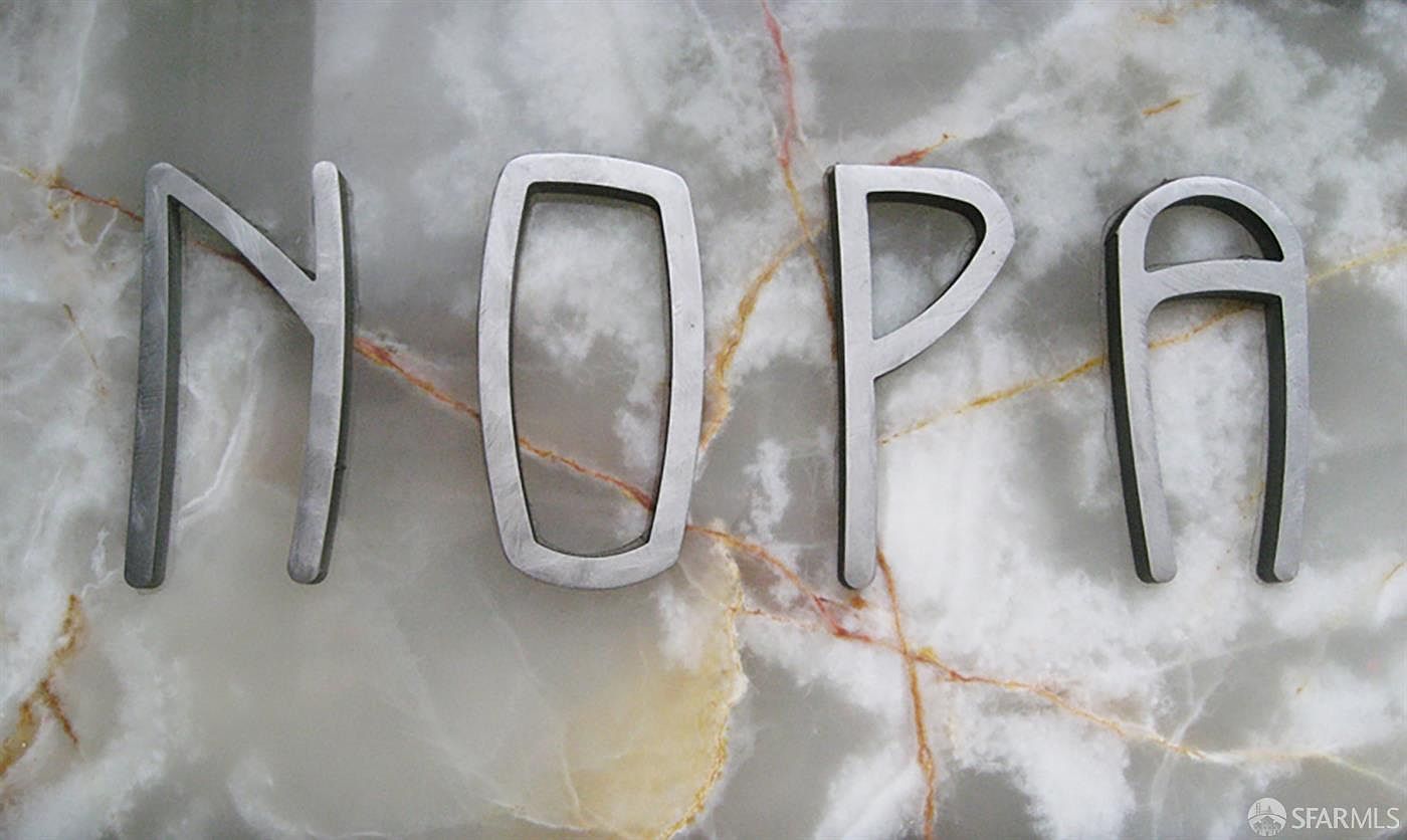 This image features the word 'NOPA' spelled out in large, metallic, three-dimensional letters mounted against a polished, light-colored marble or stone surface with subtle veining. The letters have a modern, industrial aesthetic with a clean, sans-serif font. The close-up perspective highlights the texture of the stone and the metallic finish of the signage, suggesting a sophisticated and contemporary building entrance or interior design element.