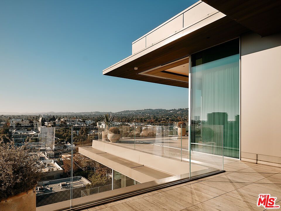 This image showcases a modern balcony with a stunning city view. The balcony features a glass railing, providing an unobstructed panorama, and is adorned with potted plants. The architectural design is sleek and contemporary, emphasizing clean lines and open space, perfect for enjoying the cityscape.