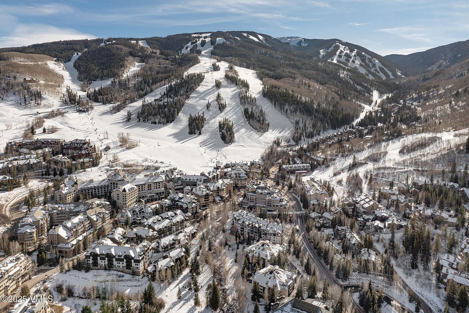 This aerial view showcases a luxurious ski resort nestled in a snow-covered mountain landscape. The scene features a cluster of upscale chalets and resort buildings, surrounded by ski slopes and evergreen forests. The overall impression is one of a high-end winter retreat, perfect for skiing enthusiasts and those seeking a scenic getaway.
