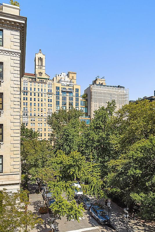 This elevated perspective captures a vibrant urban street scene framed by lush, mature trees and historic architecture. The view highlights a mix of classic masonry buildings and modern structures, including one currently undergoing exterior renovations with scaffolding. The scene provides a sense of the neighborhood's character, blending dense city living with abundant greenery.