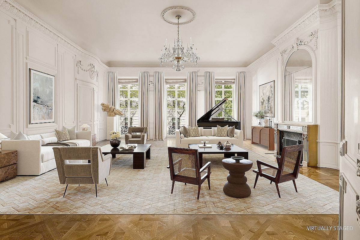 This expansive, formal living room features high ceilings with intricate crown molding and a grand crystal chandelier as the centerpiece. The space is furnished with two distinct seating areas, including plush sofas and mid-century modern style chairs, arranged on a large patterned area rug over herringbone wood floors. Tall windows with elegant drapery allow natural light to fill the room, which also includes a grand piano and a fireplace with a decorative mantel.