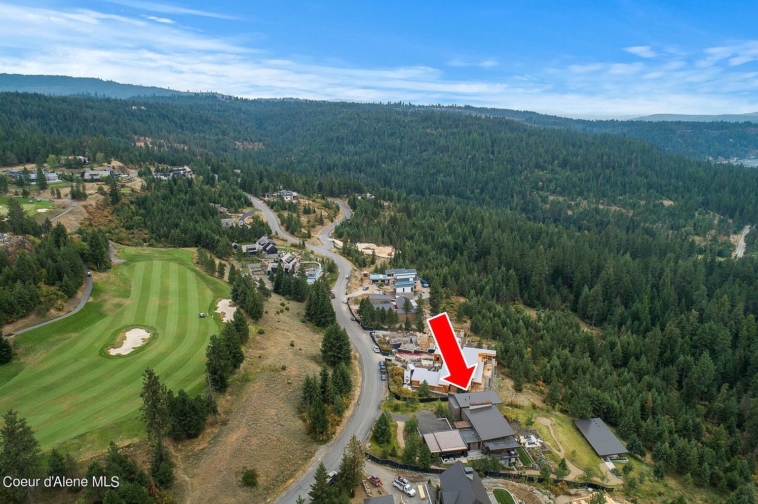 This aerial shot showcases a luxurious home nestled in a wooded area, possibly part of a golf course community. The property features a multi-level design with dark roofing and well-maintained landscaping. A winding road leads to the house, suggesting privacy and exclusivity.
