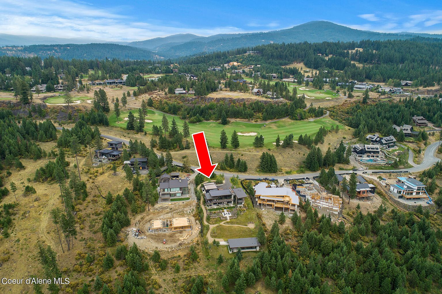 This aerial view showcases a luxurious residential area nestled amidst lush greenery and a golf course. Several modern homes are visible, some under construction, highlighting the ongoing development in this upscale community. The landscape features rolling hills and mature trees, creating a serene and exclusive atmosphere.