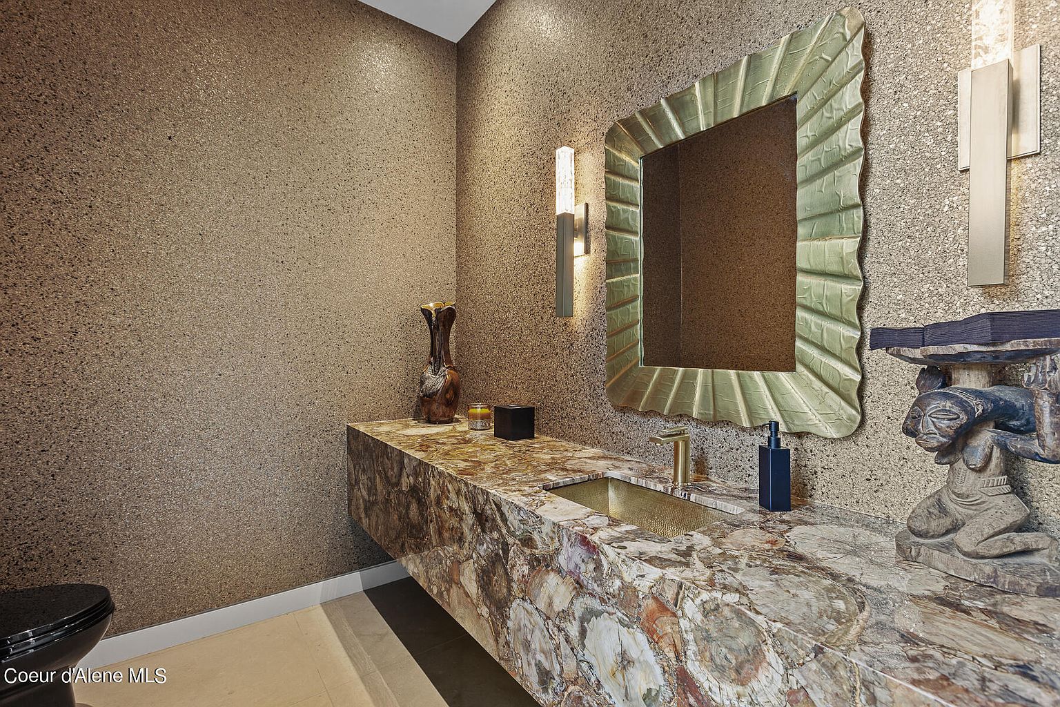 This is a stylish guest bathroom featuring a unique marble countertop with an integrated gold sink. The walls are textured, and the mirror has a leaf-like frame. An artistic statue sits on the counter, adding a touch of elegance and sophistication to the space.