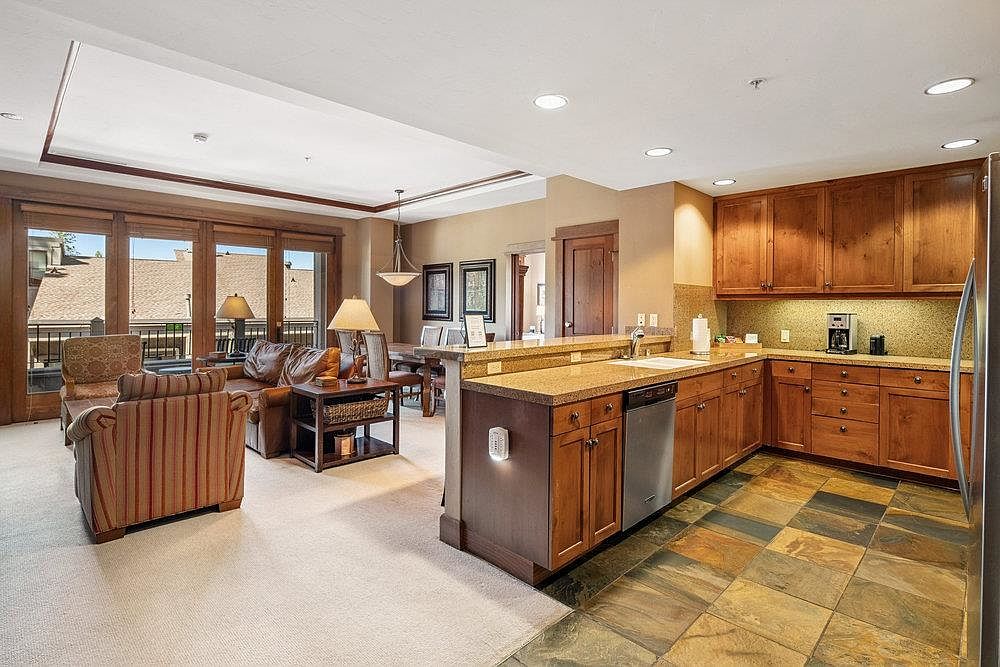This interior shot showcases a well-appointed kitchen seamlessly integrated with a living area. The kitchen features wooden cabinetry, granite countertops, and stainless steel appliances, while the living area boasts comfortable seating and access to an outdoor balcony. The open-concept design creates a warm and inviting atmosphere, perfect for entertaining.