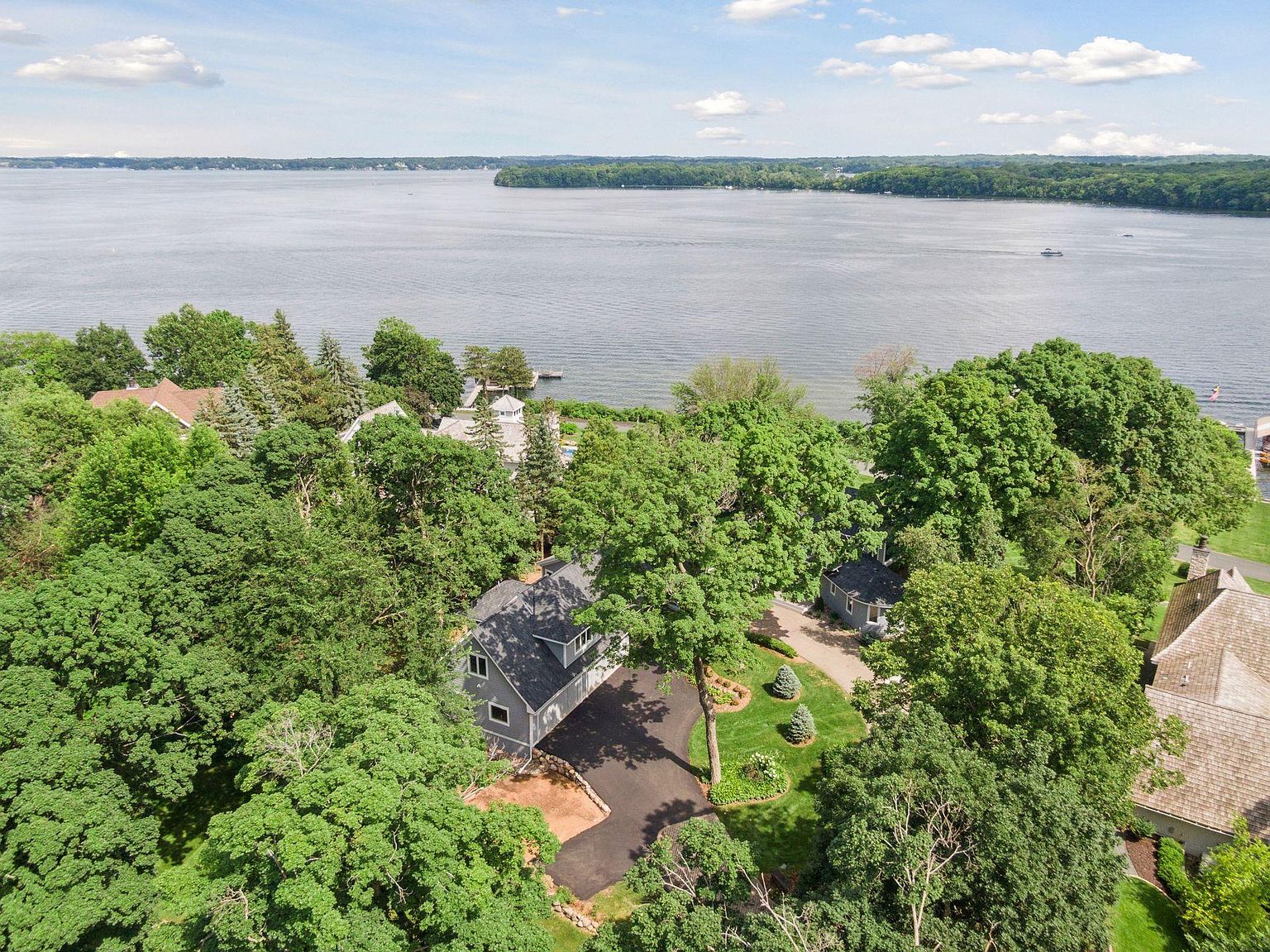 This aerial shot showcases a beautiful property nestled among lush greenery, with a view of a large body of water in the background. The house features a dark roof and a well-maintained driveway, complemented by manicured lawns and landscaping. The overall impression is one of privacy and tranquility, highlighting the property's desirable location and curb appeal.