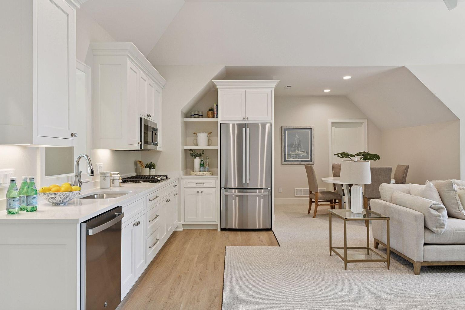 This is a bright and airy kitchen that seamlessly transitions into a living area. The kitchen features white cabinetry, stainless steel appliances, and light wood flooring, creating a clean and modern aesthetic. The open layout enhances the sense of space and connectivity, making it ideal for entertaining and family living.