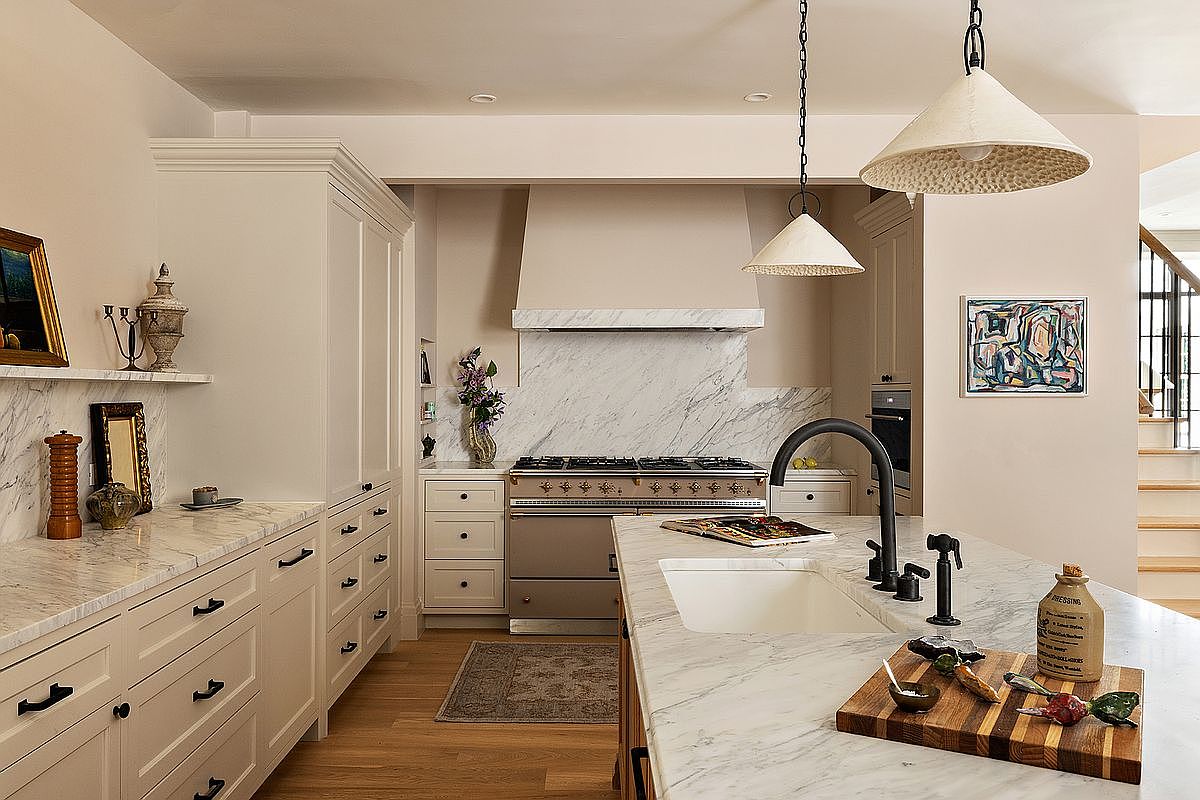 This is a well-lit kitchen featuring custom cabinetry, marble countertops, and high-end appliances. The kitchen island is the focal point, with a farmhouse sink and stylish faucet. The overall design is elegant and functional, creating a welcoming space for cooking and entertaining.