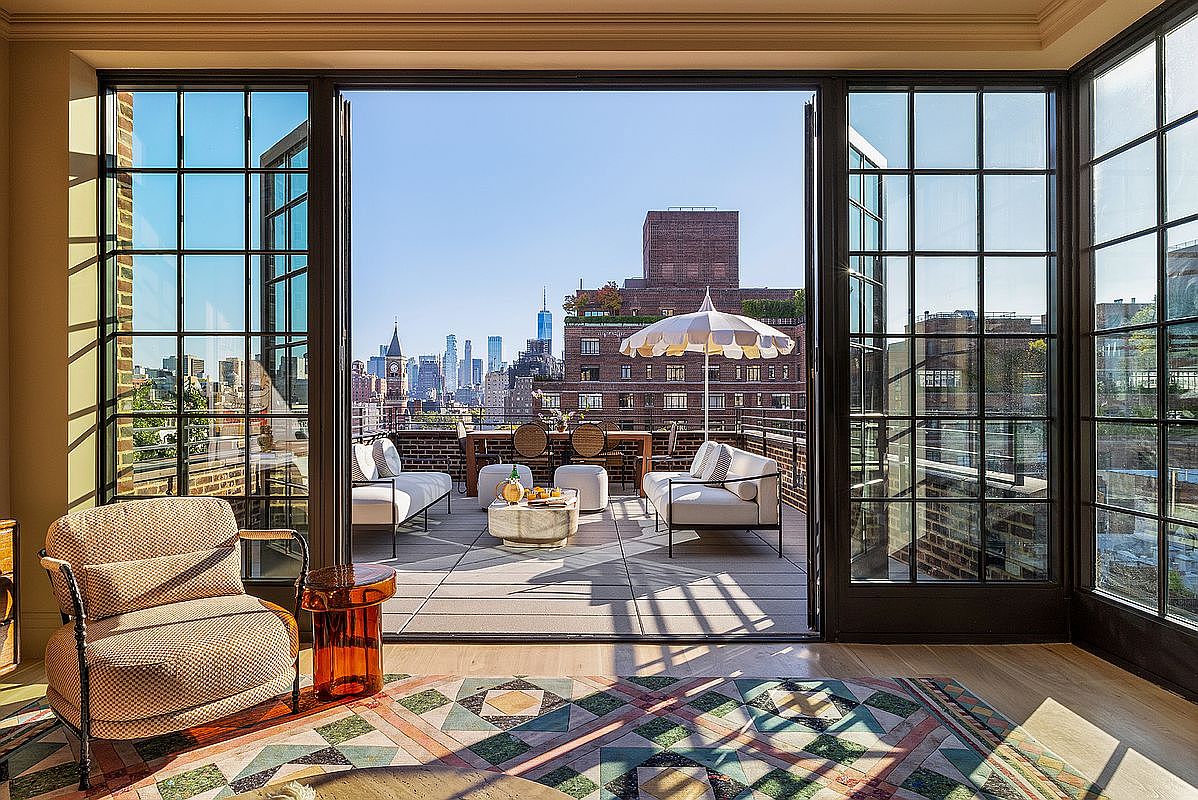 This image showcases a luxurious living room that seamlessly transitions to an expansive outdoor patio/deck. The interior features a stylish armchair and a colorful rug, while the patio boasts comfortable seating, a coffee table, and an umbrella, all set against a stunning city skyline. The open doors create an inviting indoor-outdoor living experience.
