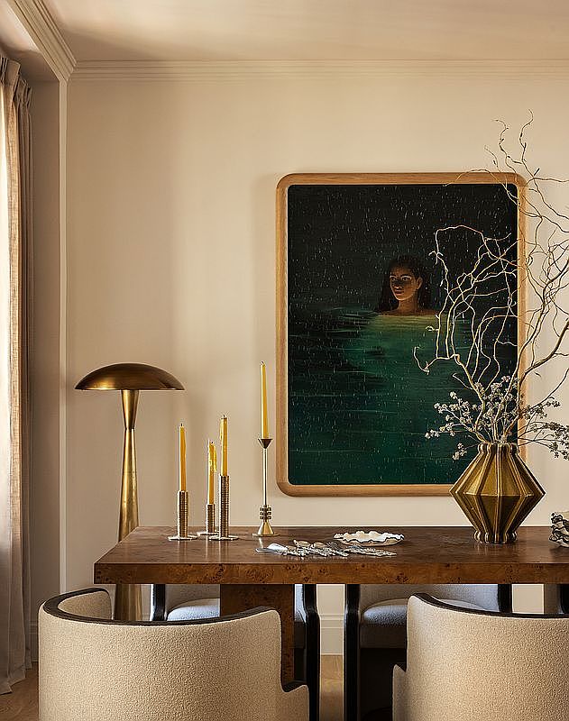 This interior shot showcases a sophisticated dining room. A wooden table is the centerpiece, adorned with candles, silverware, and a decorative vase with branches. The artwork on the wall adds a touch of elegance, while the upholstered chairs provide comfortable seating, creating an inviting atmosphere for dining and entertaining.