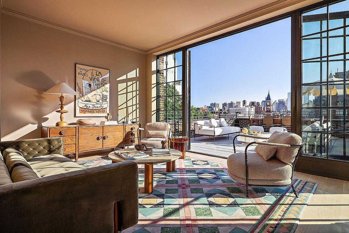 This is a stylish living room that seamlessly blends indoor and outdoor living with large sliding glass doors opening to a rooftop terrace. The interior features a comfortable sofa, armchairs, a unique patterned rug, and a mid-century modern credenza, creating a sophisticated and inviting atmosphere. The terrace offers city views, enhancing the property's appeal.