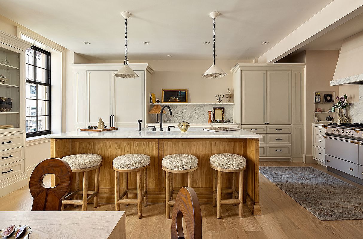 This is a well-lit kitchen featuring a large island with a wooden base and white countertop, complemented by four stools with textured cushions. The kitchen includes white cabinetry, a marble backsplash, and pendant lighting, creating a bright and inviting space. The perspective is from the front, showcasing the island as the central element.