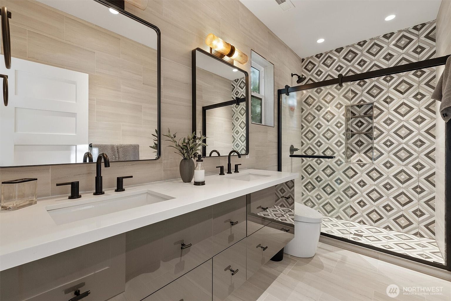 This is a well-lit primary bathroom featuring a double vanity with a white countertop and gray cabinets. Two black-framed mirrors hang above the sinks, complemented by modern black faucets and hardware. The shower area is enclosed with a black-framed glass door and showcases patterned tiles, adding a touch of elegance to the space.