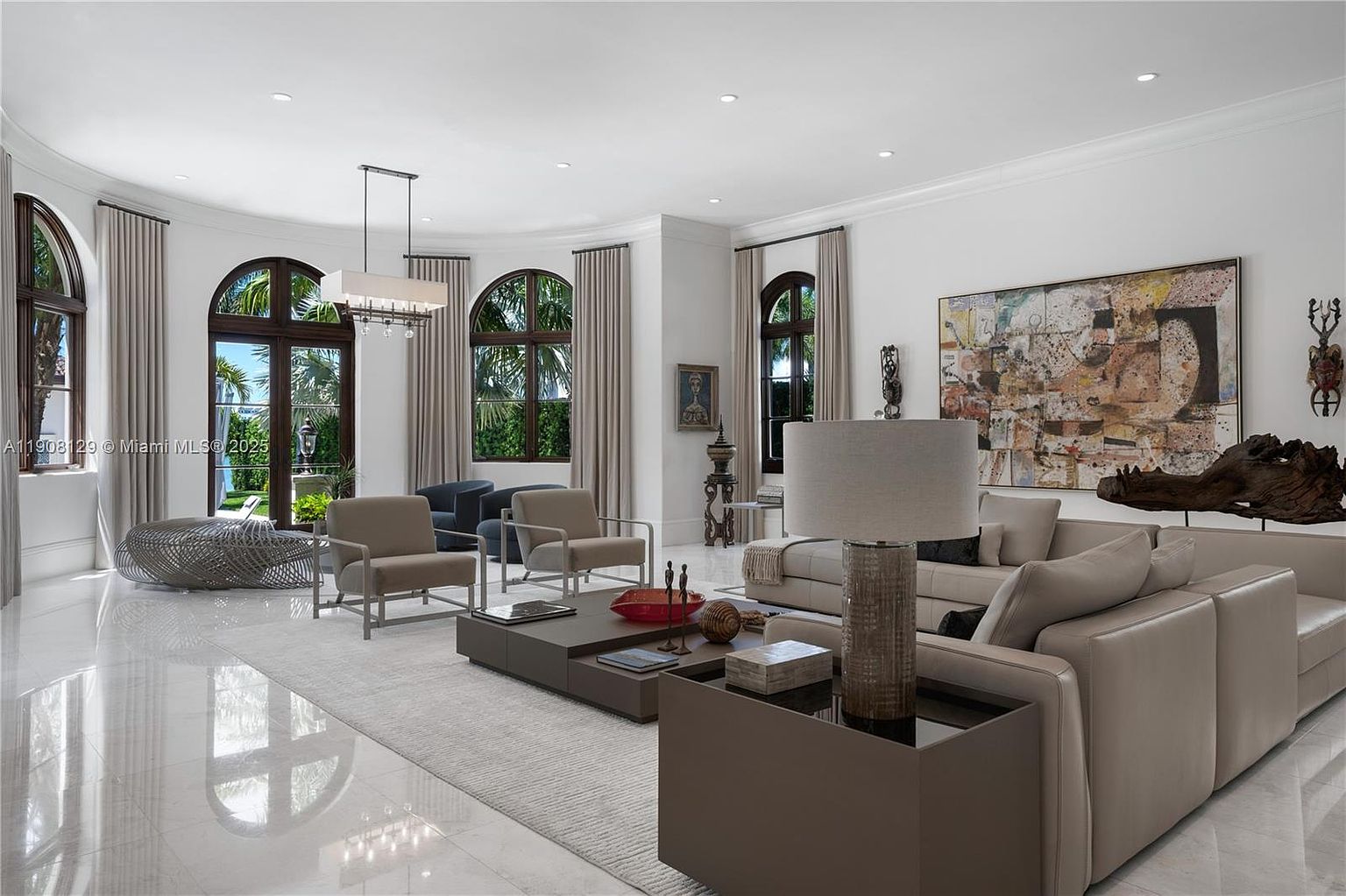 This is a spacious and luxurious living room featuring high ceilings, arched windows, and elegant decor. The room is furnished with a large sectional sofa, several armchairs, and a modern coffee table arrangement. A large abstract painting hangs on the wall, adding a touch of sophistication to the space. The perspective is from the front of the room, showcasing the entire space.