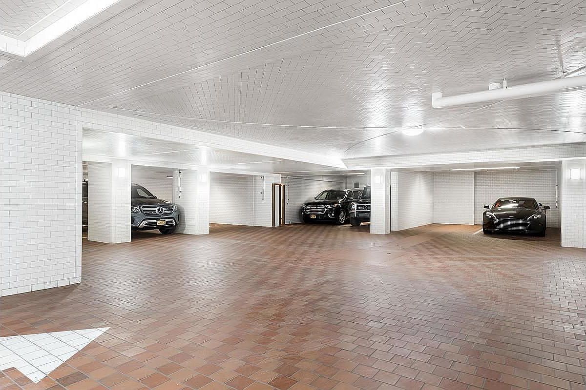 The image showcases a well-lit and spacious garage with a clean, modern aesthetic. The floor is tiled with brown bricks, while the walls and ceiling are covered in white tiles, creating a bright and airy atmosphere. Several cars are parked within the garage, highlighting its functionality and ample parking space.