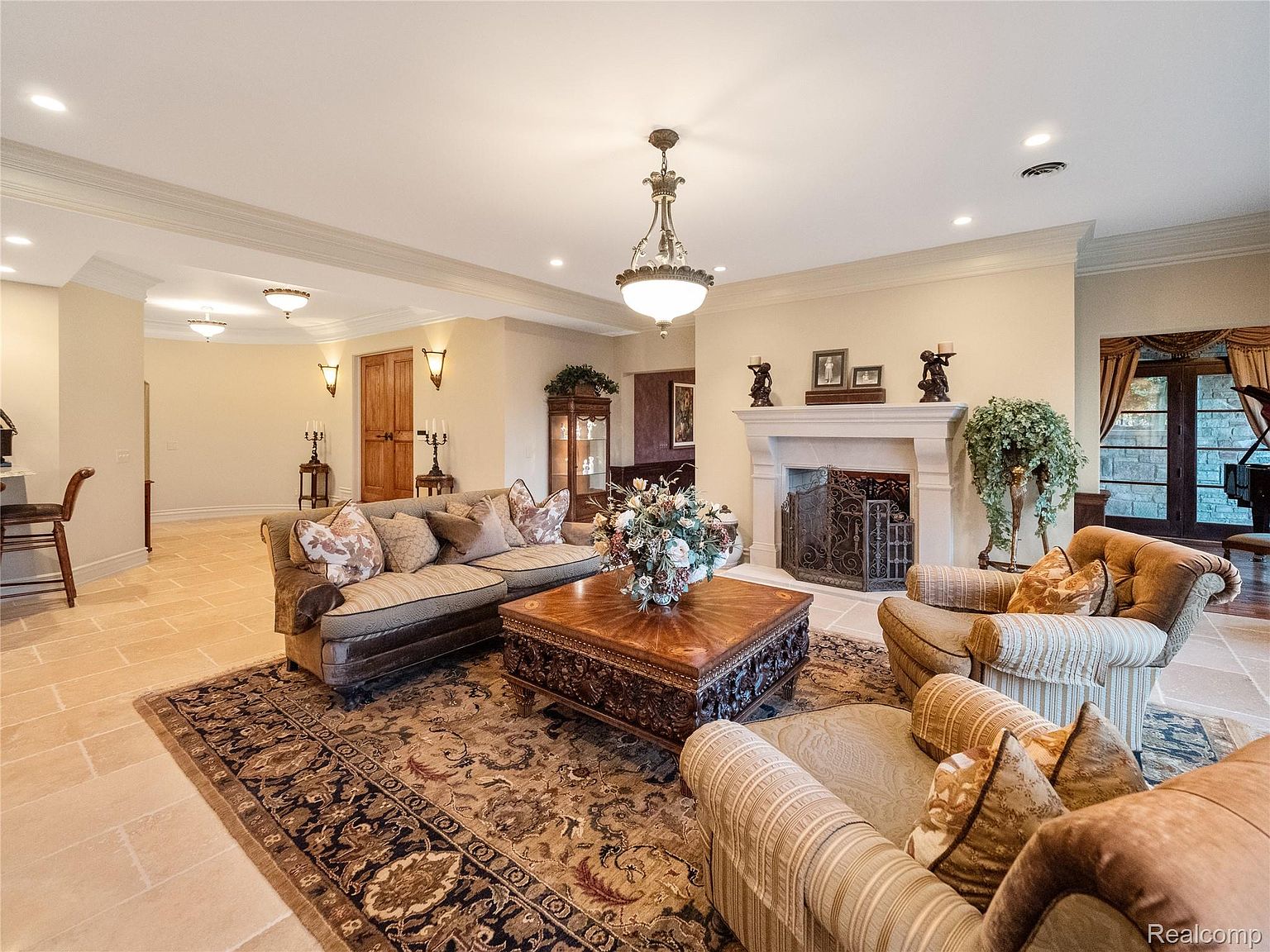 This is an interior shot of a luxurious living room featuring a large, ornate coffee table, a comfortable sofa with decorative pillows, and two armchairs. A fireplace with decorative elements adds a focal point, and an elegant chandelier illuminates the space. The room is decorated with a classic style, creating a warm and inviting atmosphere.