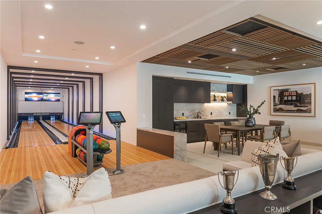 This interior shot showcases a luxurious living space that seamlessly integrates a bowling alley, a modern kitchen, and a comfortable seating area. The bowling alley features a sleek, contemporary design, while the kitchen boasts dark cabinetry and marble countertops. The living area is furnished with a plush sofa and decorative trophies, creating a sophisticated and entertaining atmosphere.