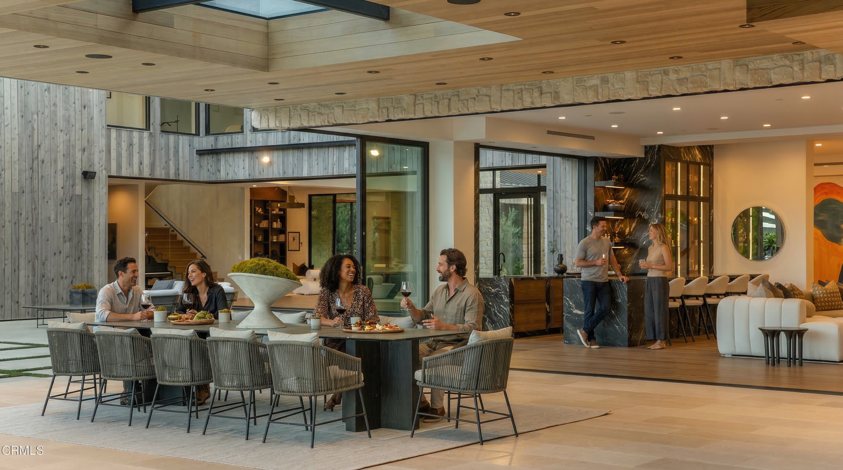 This elegant, open-concept dining area features a sleek modern table surrounded by wicker chairs, perfect for sophisticated entertaining. The space seamlessly integrates with a luxury kitchen and living area, showcasing high-end materials like natural wood ceilings and stone accents. Large, retractable glass walls blur the line between indoor and outdoor living, creating an airy, refined atmosphere ideal for a high-end estate.