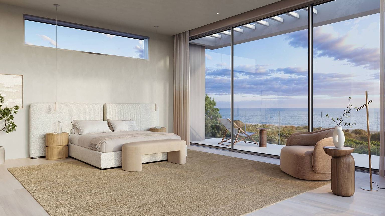 This luxurious primary bedroom features a minimalist, contemporary aesthetic with a neutral color palette and soft textures. The room is anchored by a large bed with a textured headboard, complemented by a curved accent chair and a bench at the foot of the bed. Expansive floor-to-ceiling windows provide an unobstructed, panoramic view of the ocean and coastline, creating a serene and sophisticated atmosphere.