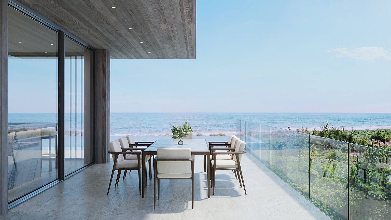 This modern, covered balcony offers a seamless transition between indoor and outdoor living with its expansive glass sliding doors and sleek, minimalist design. The space is furnished with a contemporary dining set, featuring a stone-topped table and upholstered chairs, perfectly positioned to take advantage of the unobstructed ocean views. A glass railing ensures an open, airy feel, while the wood-paneled ceiling and stone flooring add a touch of natural texture to this sophisticated coastal retreat.