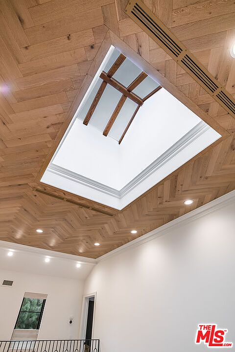 The image showcases a unique architectural detail: a ceiling adorned with herringbone-patterned wood panels and a rectangular skylight. The skylight is framed with white trim and reveals wooden beams above, creating a striking contrast. Recessed lighting adds to the ambiance, highlighting the craftsmanship and design.