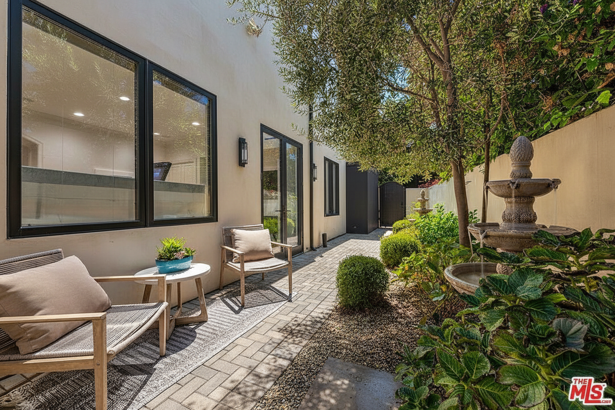 This exterior shot showcases a charming courtyard or garden area. Features include a decorative fountain, meticulously maintained landscaping, and comfortable seating arrangements. The brick pathway adds texture, and the overall ambiance suggests a peaceful and inviting outdoor space.