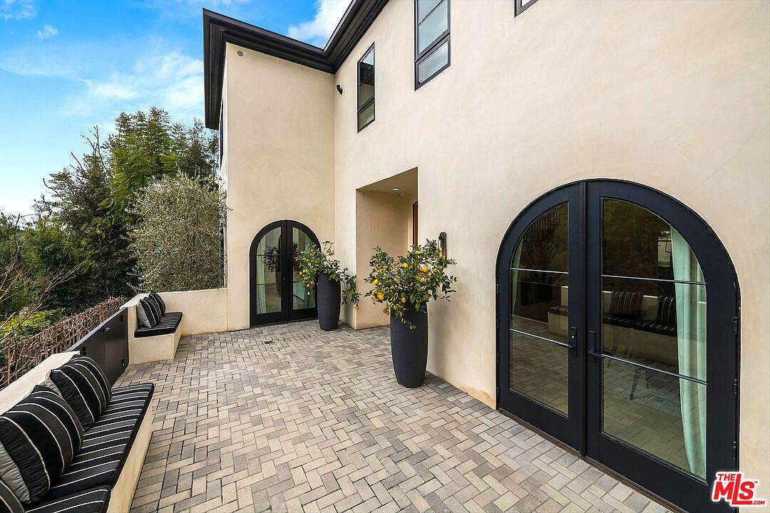 This image showcases a stylish patio area with a herringbone brick floor, complemented by built-in benches with striped cushions. The exterior of the building features arched doorways and windows, adding architectural interest. Potted lemon trees provide a touch of greenery and color, enhancing the overall aesthetic of the outdoor space.