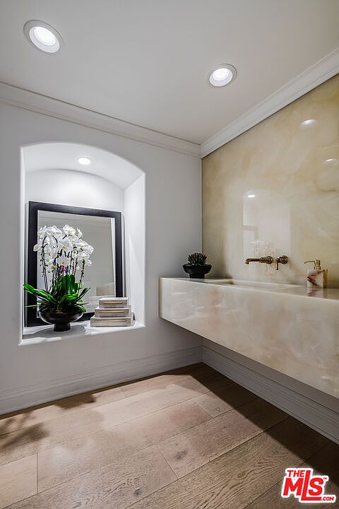 This is a well-lit bathroom featuring a modern, floating vanity with a marble countertop and backsplash. A decorative niche houses a floral arrangement and stacked boxes, adding a touch of elegance. The warm wood flooring complements the cool tones of the marble, creating a sophisticated and inviting space.