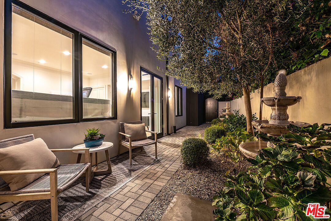 This image showcases a beautifully landscaped side yard or garden area. The space features a brick pathway, gravel accents, lush greenery, and a tiered fountain, creating a serene and inviting atmosphere. Outdoor seating is arranged near the building, suggesting a relaxing space for residents.