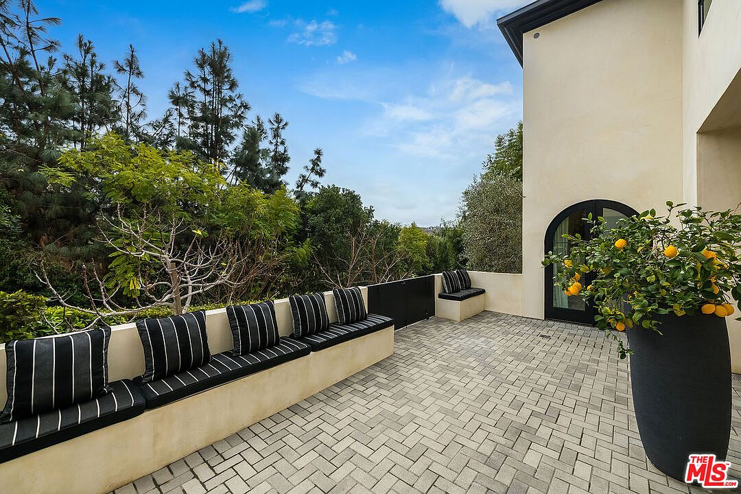 This image showcases a stylish outdoor patio area, featuring a long built-in bench with striped cushions and a smaller matching bench near an arched doorway. The patio is paved with herringbone-patterned bricks, and a large potted lemon tree adds a touch of greenery and vibrancy. The overall impression is one of a sophisticated and inviting outdoor living space.