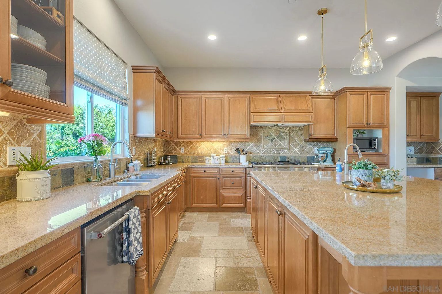 This is a well-lit kitchen featuring wooden cabinetry, granite countertops, and stainless steel appliances. The kitchen includes a central island with ample counter space and pendant lighting. The overall impression is one of warmth and functionality, ideal for both cooking and entertaining.