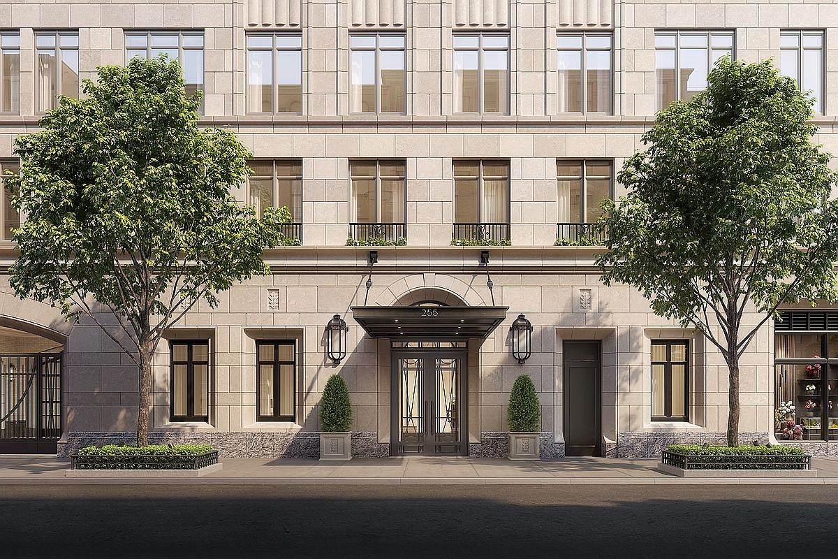This elegant, symmetrical building facade features a sophisticated stone exterior with a prominent, classic entryway marked by the number 255. The entrance is framed by a dark metal canopy, flanked by matching wall-mounted lanterns and manicured topiary planters, creating a refined and welcoming street-level presence. Two mature trees frame the composition, adding a touch of natural greenery to the formal architectural design.